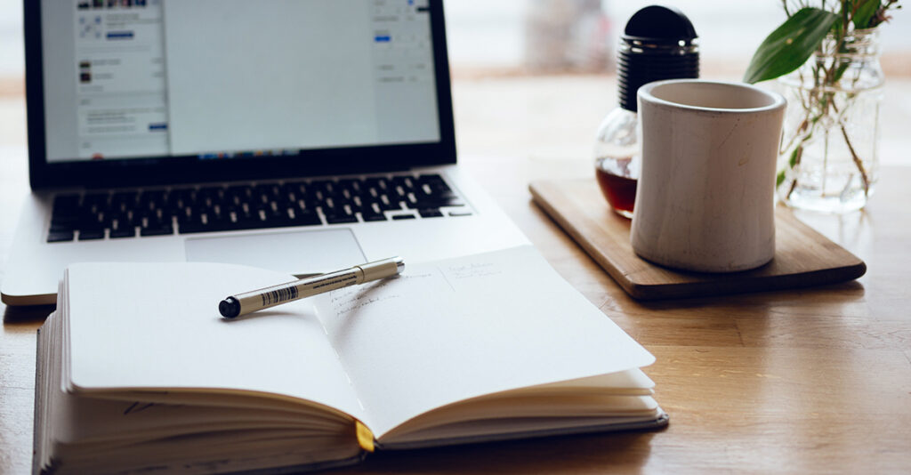 Open notebook on table with a cup of coffee.