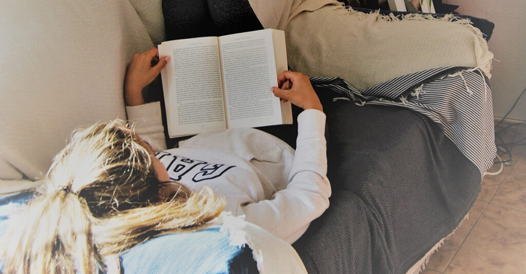 Woman laying down reading book on couch